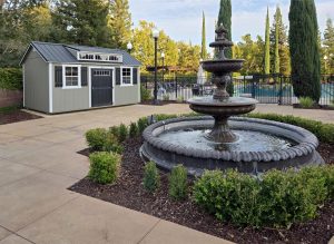 A Utility Shed with a Shed Dormer package nearby a spring fountain and local community pool.