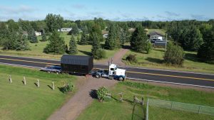 Old Hickory Lofted Barn with black roof and black siding delivered by truck and trailer in scenic residential area